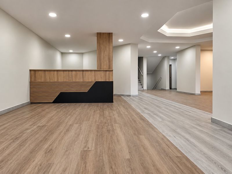 Modern, spacious office reception area featuring a custom wood-accented desk, recessed lighting, and high-quality laminate flooring throughout.