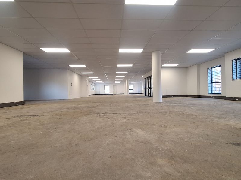 A spacious, open-plan office area featuring a suspended ceiling, recessed lighting, and structural columns, currently awaiting final flooring installation.