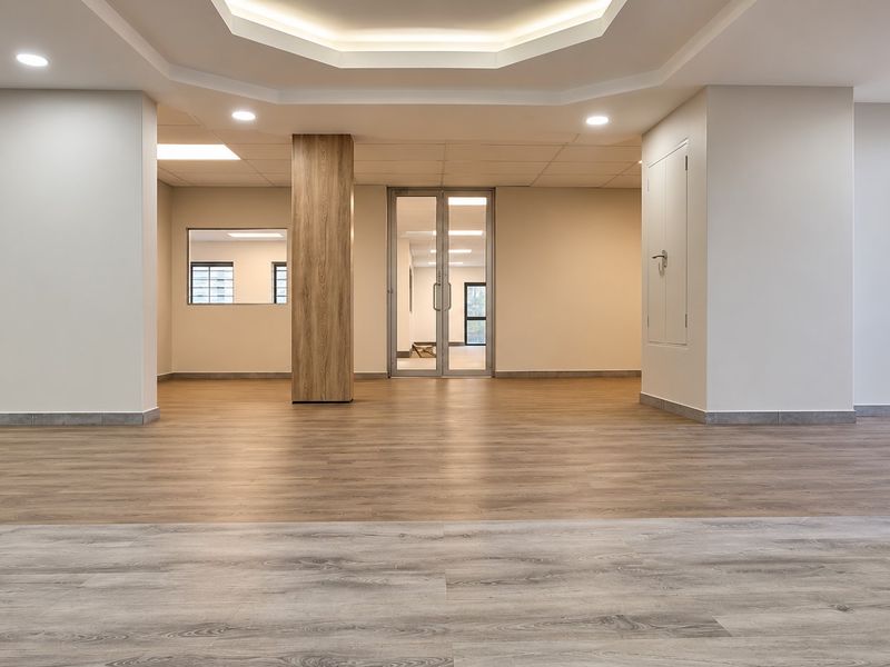 A spacious, modern open-plan office area featuring wood-look flooring, recessed lighting, and a central wood-clad column, offering a clean and professional workspace.