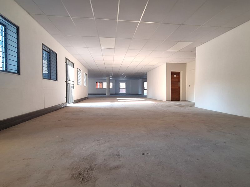A spacious, open-plan office area featuring a suspended ceiling, security-barred windows, and unfinished concrete flooring, offering a blank canvas for custom fit-outs.