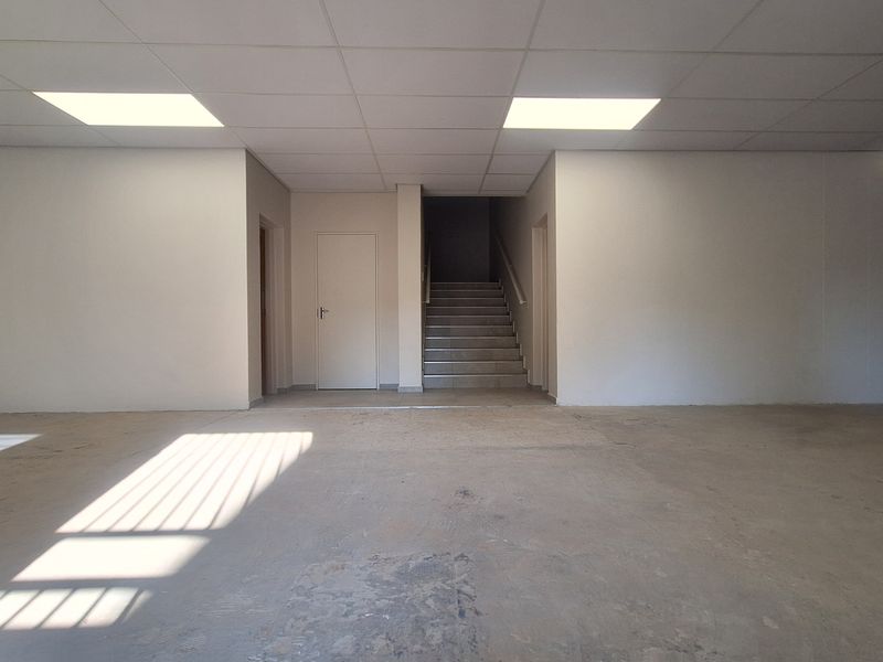 An open-plan office space featuring a suspended ceiling with recessed lighting, concrete flooring, and an internal staircase leading to another level.