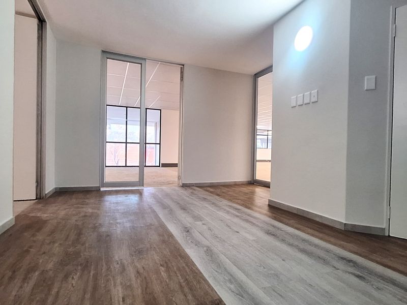 A bright, vacant office space featuring modern laminate flooring, glass partition doors, and clean white walls, ready for professional fit-out.