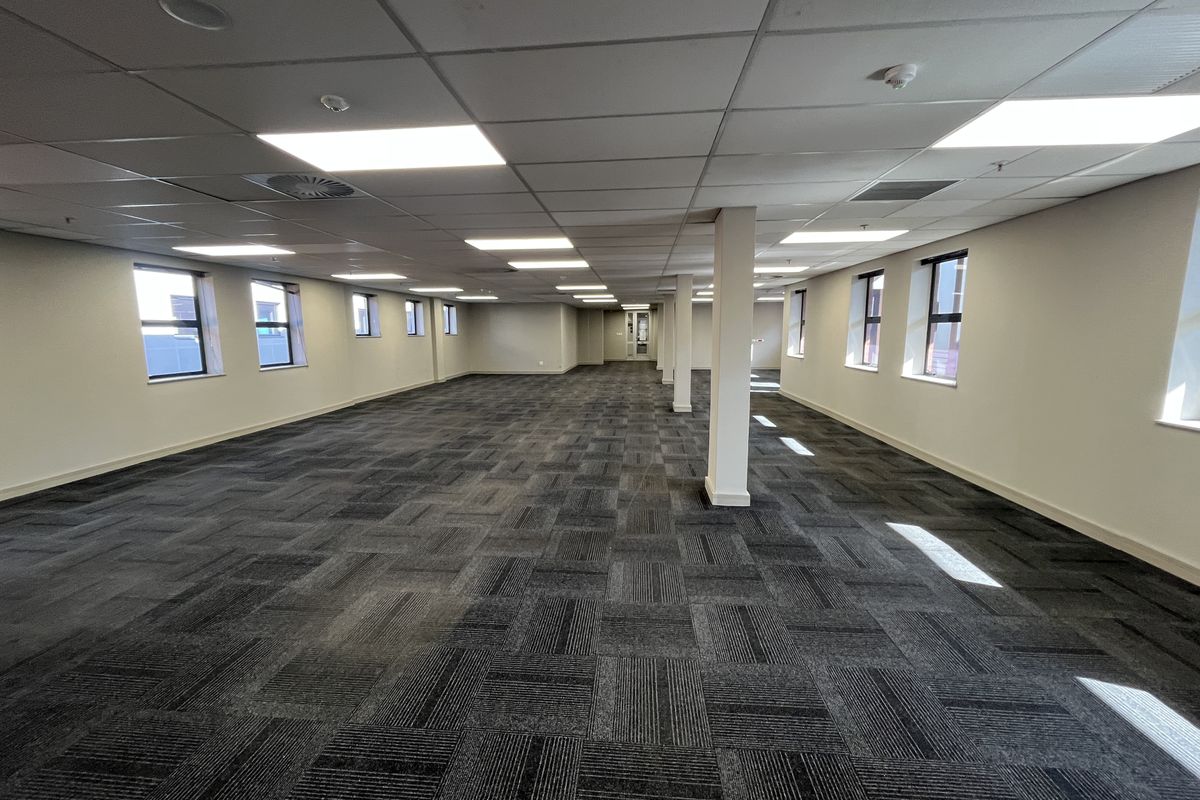 A spacious, open-plan office area featuring a suspended ceiling, recessed lighting, and modern carpet tiles, providing a clean and professional workspace.