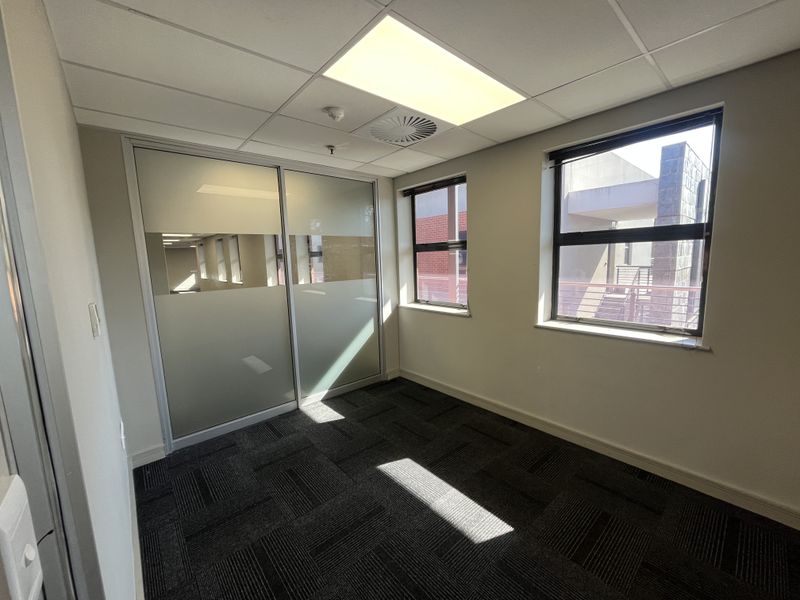 A clean, empty office space featuring carpet tiles, a suspended ceiling with recessed lighting, and a frosted glass sliding partition.