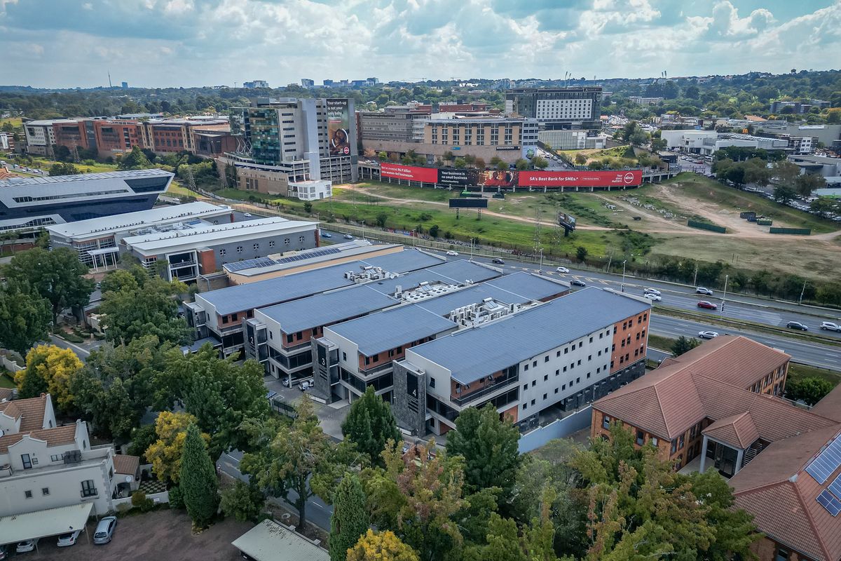 Aerial view of a modern multi-story office park complex featuring rooftop solar panels and HVAC systems, situated in a well-developed commercial area.