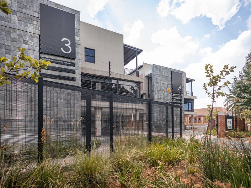 Modern commercial office building facade featuring stone cladding, glass curtain walls, and secure perimeter fencing with integrated electric security systems.
