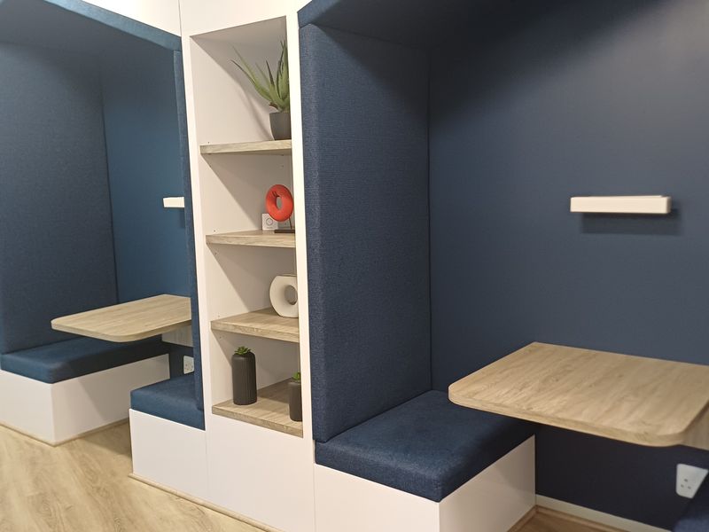 Modern office space featuring built-in acoustic work pods with integrated shelving and wall-mounted desks, providing a functional and contemporary workspace solution.