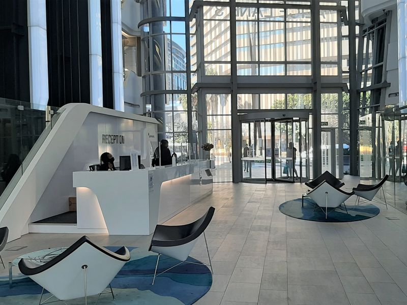 Modern office building entrance lobby featuring a sleek reception desk, expansive floor-to-ceiling glass facade, and high-quality tiled flooring.