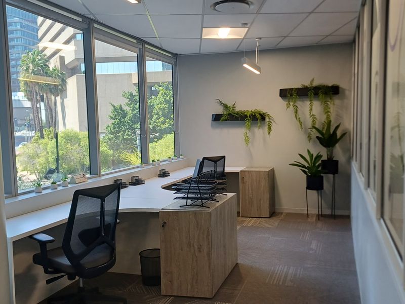 A bright, modern office space featuring a large built-in desk, expansive windows with natural light, and professional carpeted flooring.