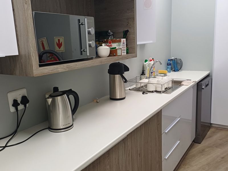 A modern office kitchenette featuring wood-grain and white cabinetry, a stainless steel sink, integrated dishwasher, and built-in microwave.