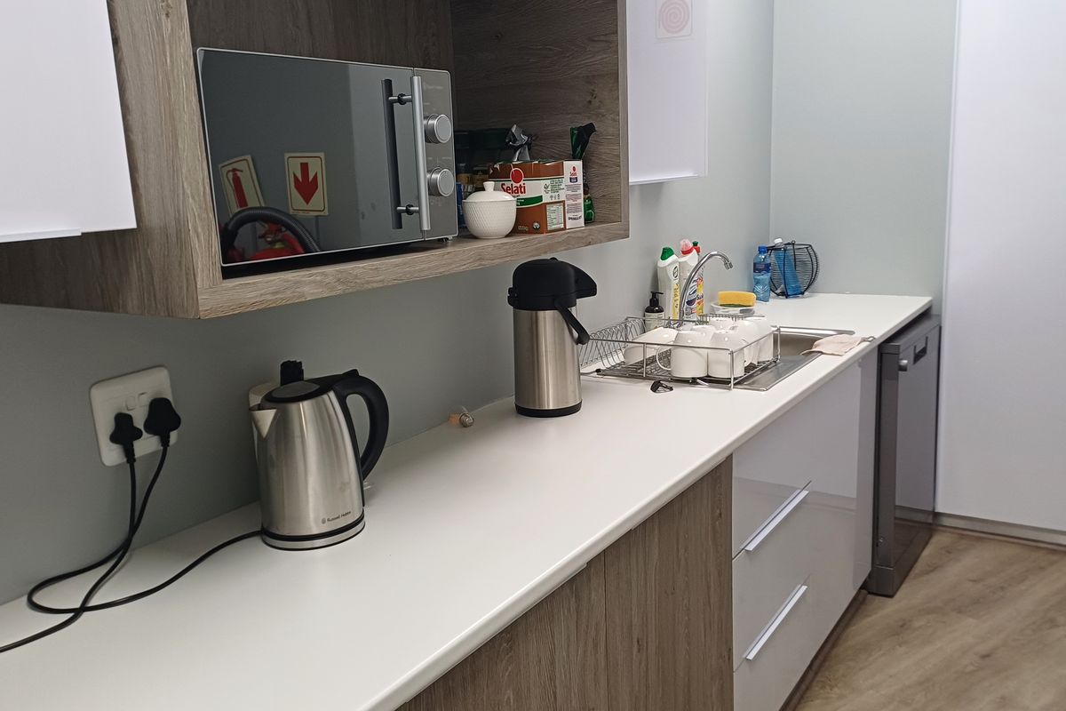 A modern office kitchenette featuring wood-grain and white cabinetry, a stainless steel sink, integrated dishwasher, and built-in microwave.