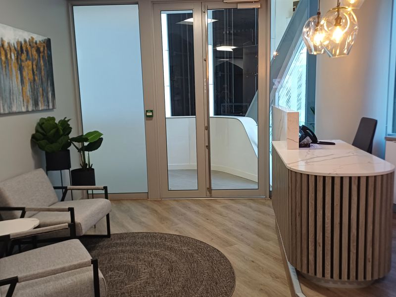 Modern office reception area featuring a contemporary slatted reception desk, glass-panelled entry doors, and high-quality laminate flooring.
