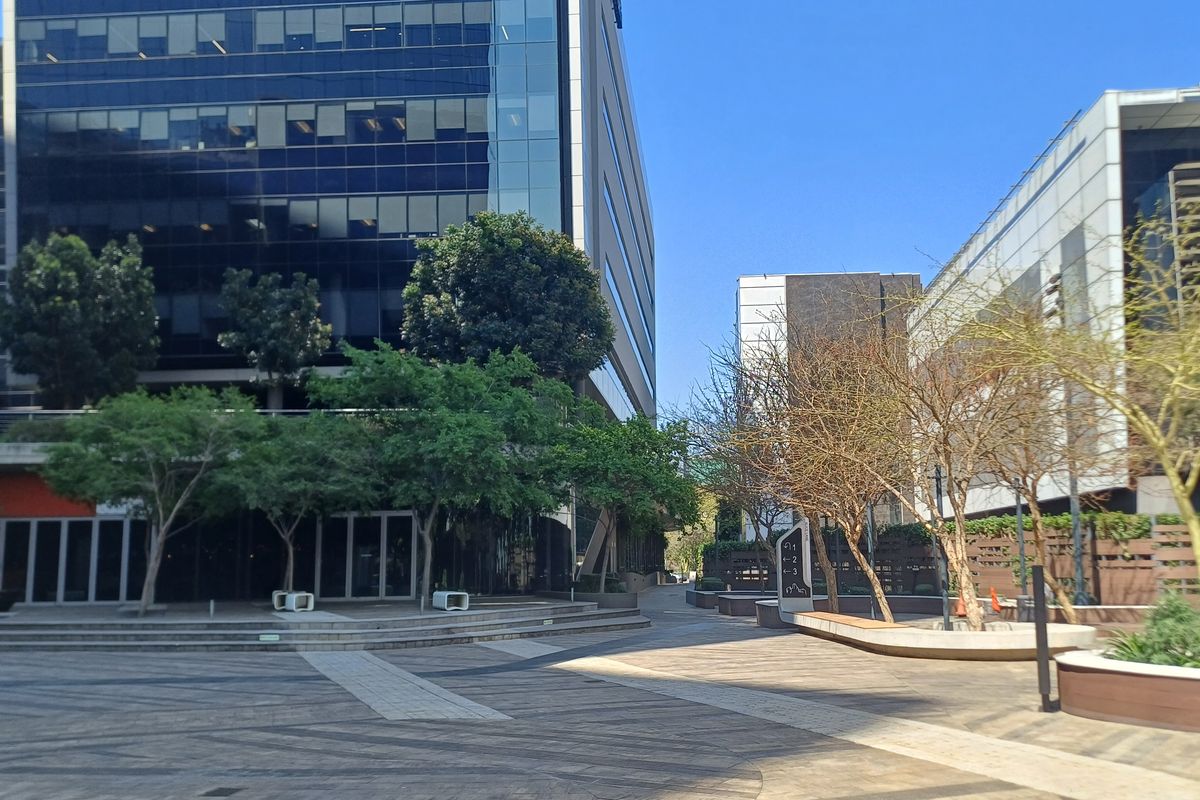 A well-maintained paved courtyard area between modern office buildings, featuring landscaped planters, glass facades, and clear directional signage.
