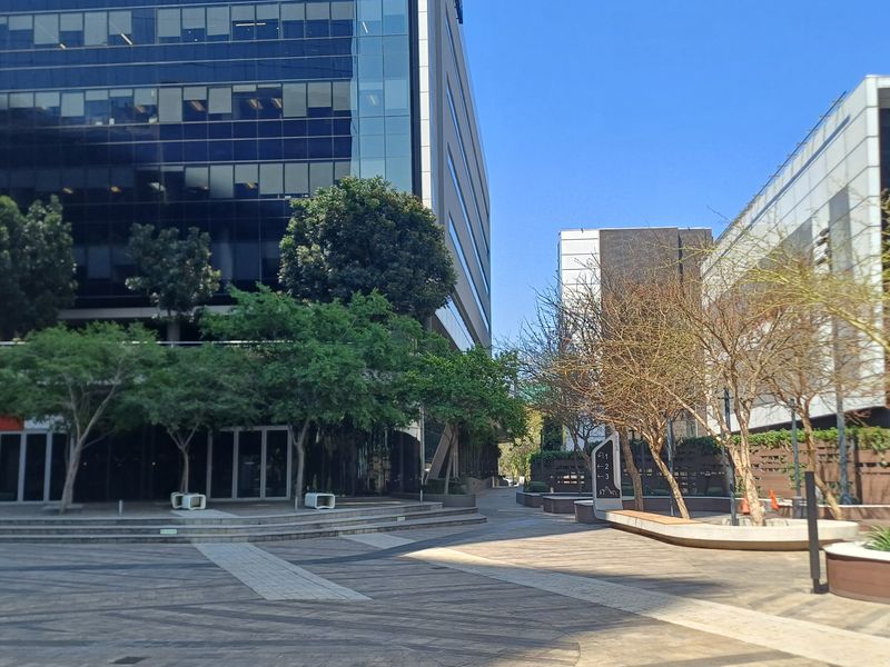 A well-maintained paved courtyard area between modern office buildings, featuring landscaped planters, glass facades, and clear directional signage.