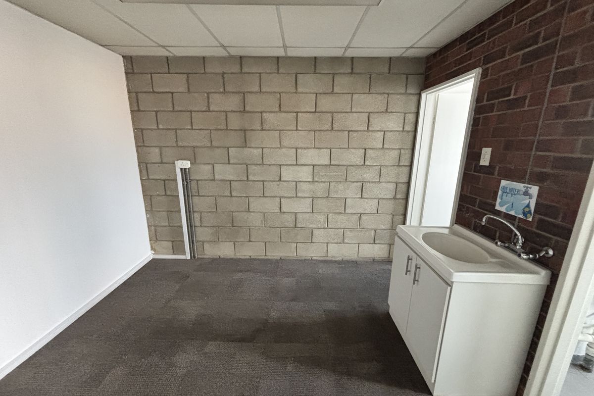 A functional utility space featuring an exposed brick and concrete block wall, drop ceiling, and a built-in vanity sink.