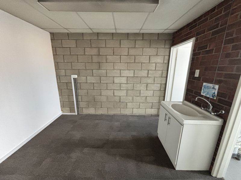 A functional utility space featuring an exposed brick and concrete block wall, drop ceiling, and a built-in vanity sink.