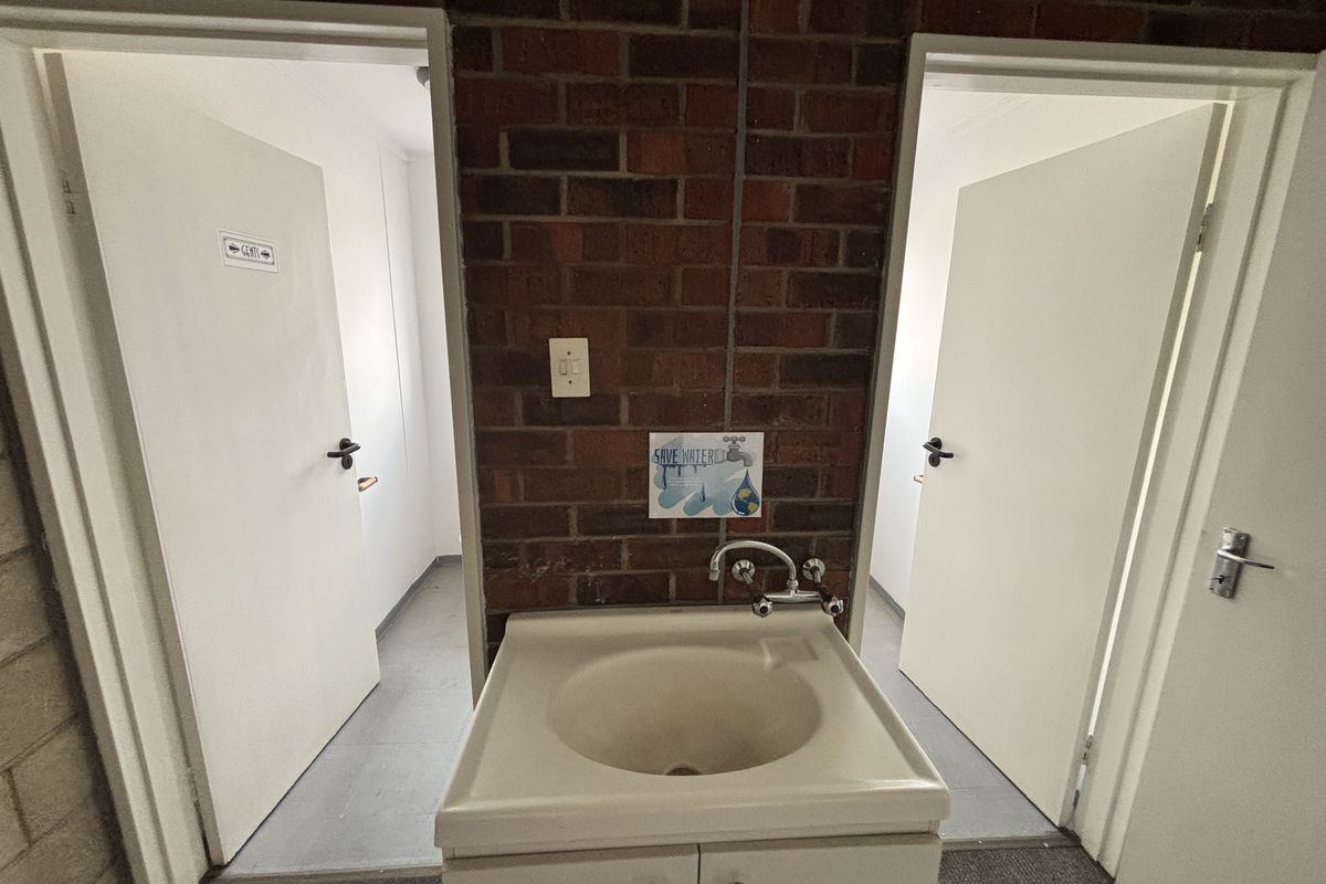 A functional industrial-style wash area featuring an exposed brick wall, pedestal basin, and dual access doors to separate restroom facilities.
