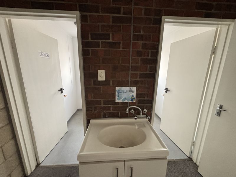 A functional industrial-style wash area featuring an exposed brick wall, pedestal basin, and dual access doors to separate restroom facilities.