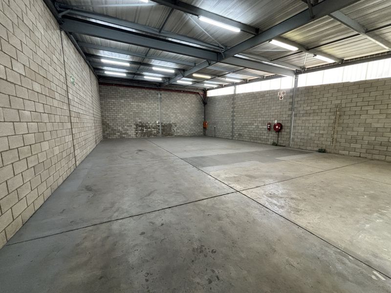 Spacious industrial utility area featuring exposed steel roof trusses, concrete flooring, and block walls, equipped with essential fire safety infrastructure.