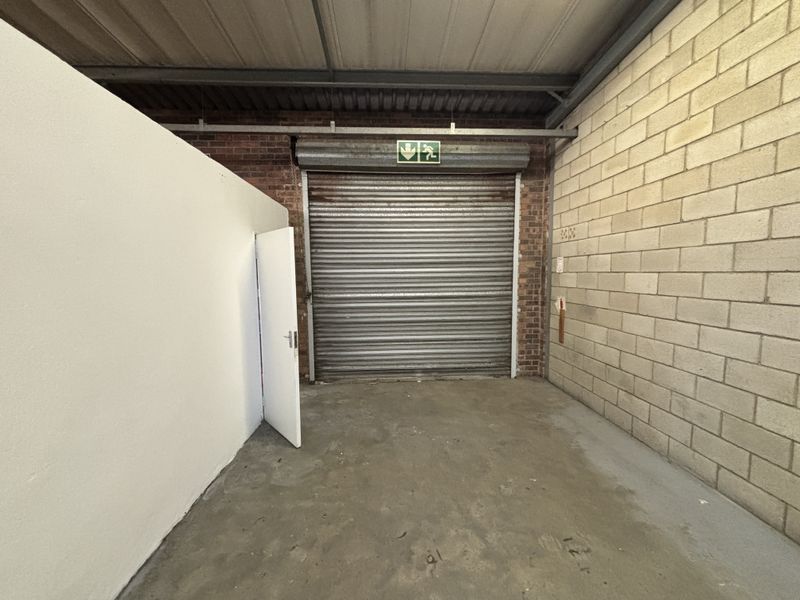 Industrial garage space featuring a roller shutter door, exposed brick and block walls, and durable concrete flooring, suitable for storage or workshop use.