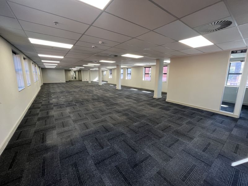 A spacious, open-plan office area featuring a suspended ceiling, recessed lighting, and durable carpet tiles, providing a clean and professional workspace.