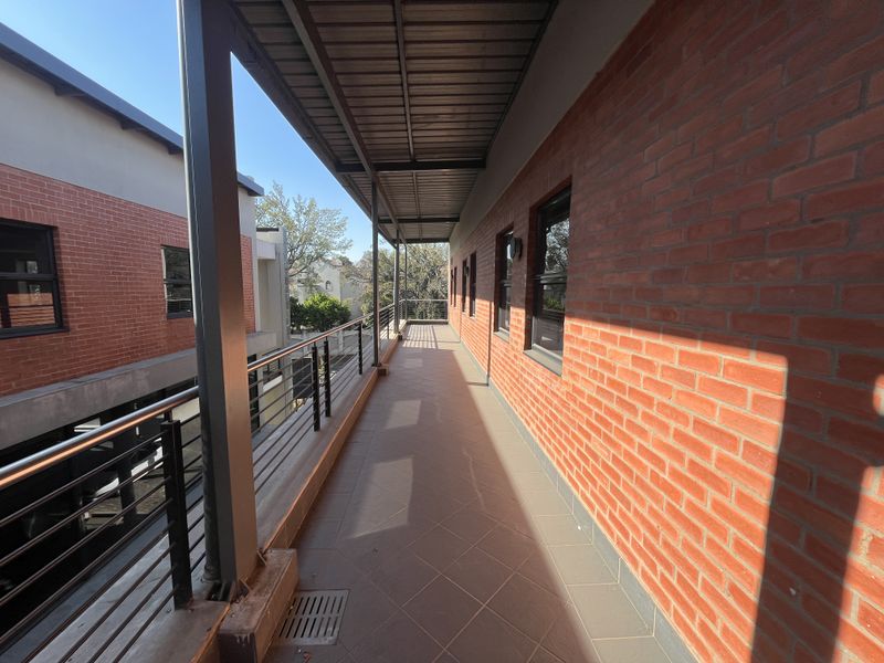A spacious, covered outdoor balcony featuring exposed brick walls, tiled flooring, and a modern metal railing, providing a clean and well-maintained exterior walkway.