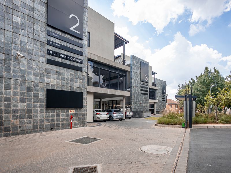 Modern office complex exterior featuring stone cladding, large glass windows, and a paved driveway with clear signage for multiple corporate tenants.
