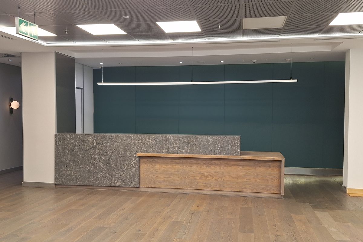 Modern office reception area featuring a stone and wood-paneled reception desk, hardwood flooring, and a professional suspended ceiling with integrated lighting.