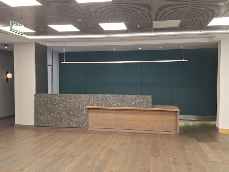 Modern office reception area featuring a stone and wood-paneled reception desk, hardwood flooring, and a professional suspended ceiling with integrated lighting.