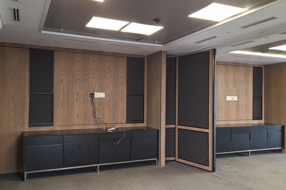 Modern office space featuring high-quality wood paneling, built-in black cabinetry, recessed ceiling lighting, and integrated floor power outlets in a professional setting.