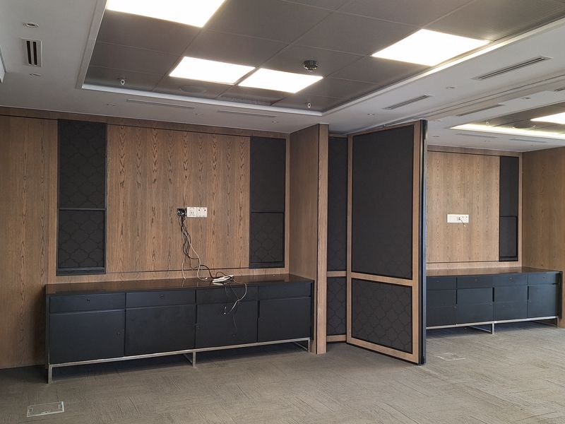 Modern office space featuring high-quality wood paneling, built-in black cabinetry, recessed ceiling lighting, and integrated floor power outlets in a professional setting.