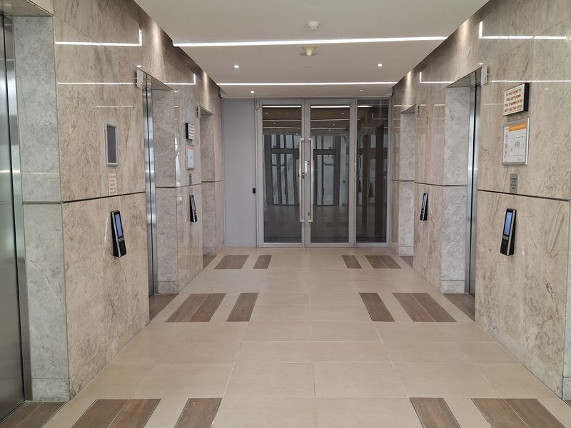 A modern, well-maintained office building elevator lobby featuring marble wall finishes, recessed lighting, and high-quality ceramic floor tiling.