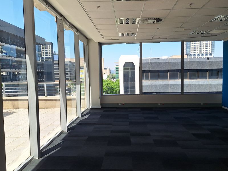 A bright, vacant office space featuring floor-to-ceiling windows, carpet tiles, and a modern suspended ceiling with integrated lighting and air conditioning.