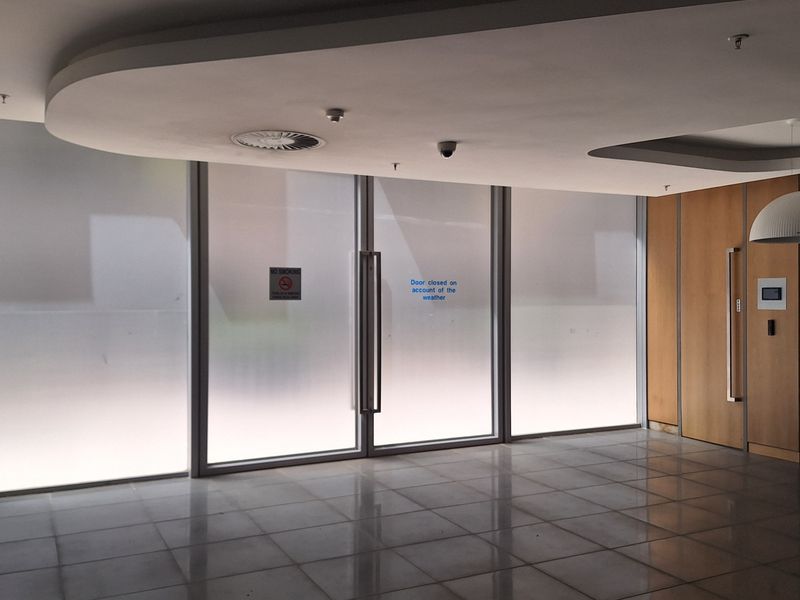 A modern office entrance area featuring polished tiled floors, a recessed ceiling design, and frosted glass doors with wood-paneled accents.