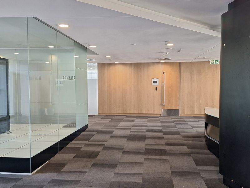 A modern, professional office lobby featuring glass partitions, timber wall paneling, and neutral carpet tiles, creating a clean and contemporary workspace environment.