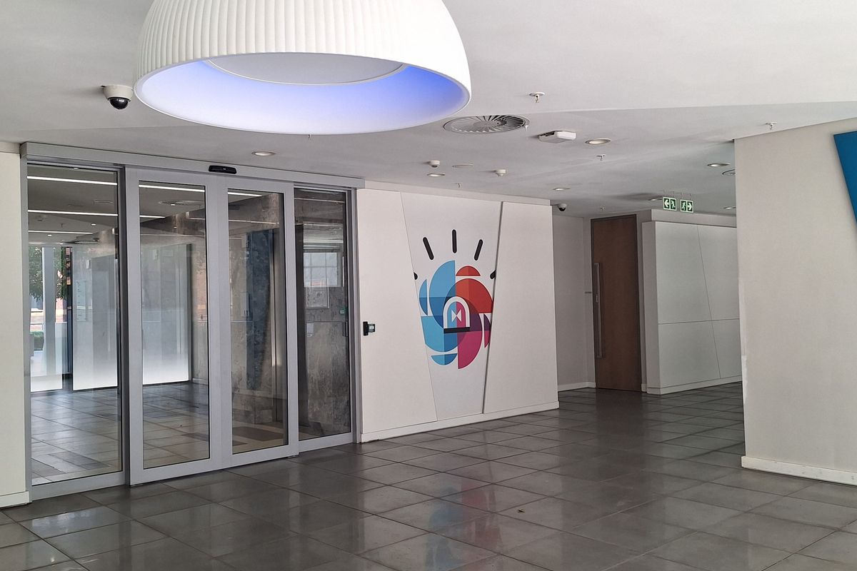 Modern office entrance lobby featuring large sliding glass doors, polished tiled flooring, and contemporary recessed and pendant lighting.