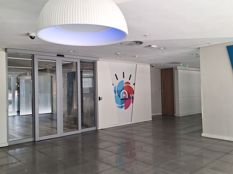 Modern office entrance lobby featuring large sliding glass doors, polished tiled flooring, and contemporary recessed and pendant lighting.