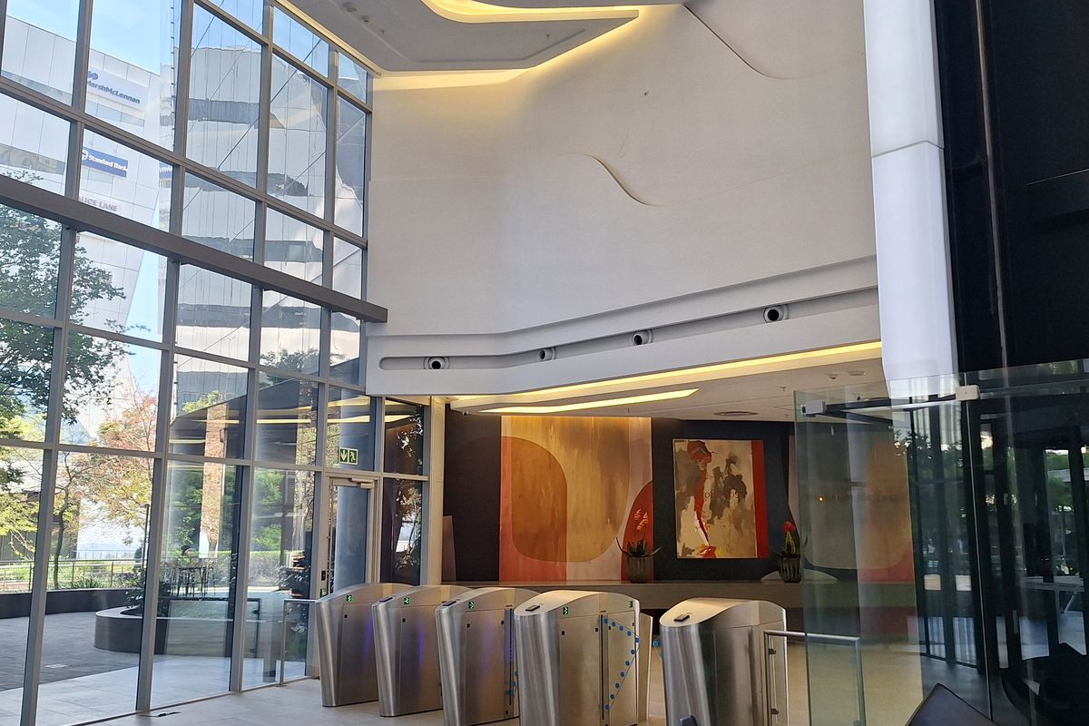 Modern office building lobby featuring a double-volume glass facade, integrated security turnstiles, and sophisticated architectural ceiling lighting.