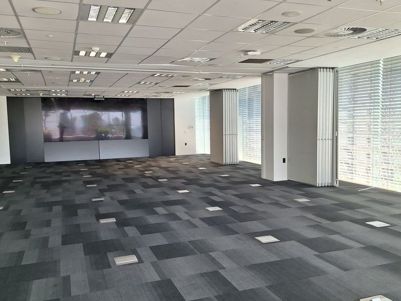 Spacious open-plan office area featuring a suspended ceiling, recessed lighting, carpet tiles, floor power access points, and a built-in media wall.