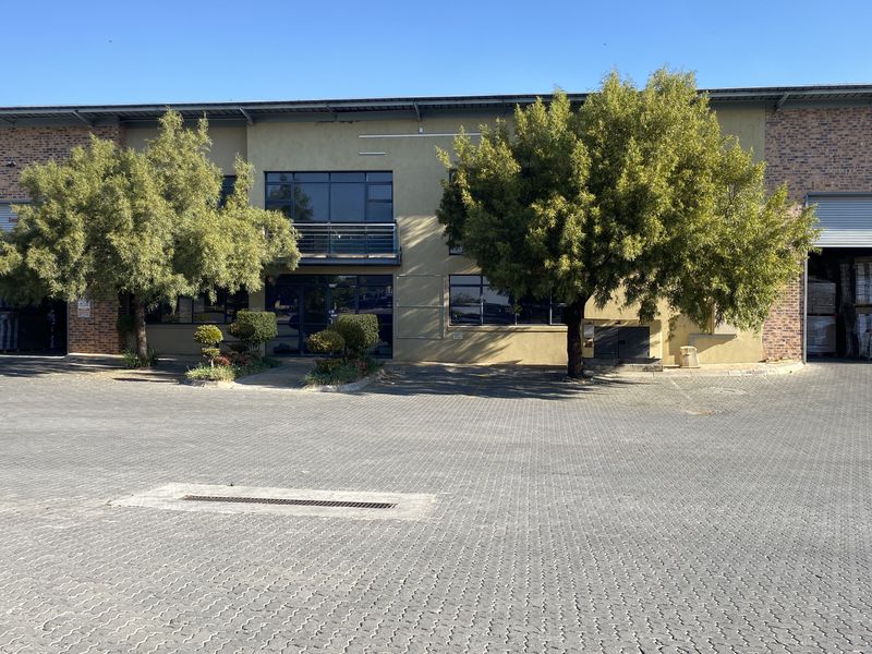 Front elevation of an industrial property featuring a paved driveway, roller shutter doors, and a brick and plaster facade.