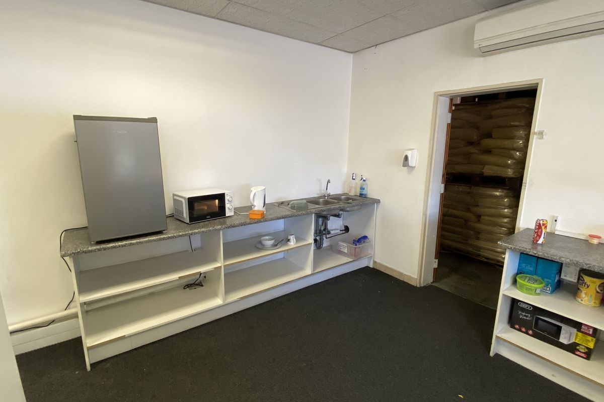 A functional industrial kitchenette featuring a stainless steel sink, laminate countertops, open shelving, and a wall-mounted air conditioning unit.