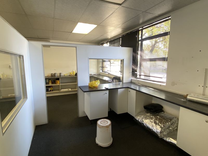 Functional office space featuring built-in cabinetry, laminate countertops, and an internal glass partition, offering a practical layout for industrial or commercial use.