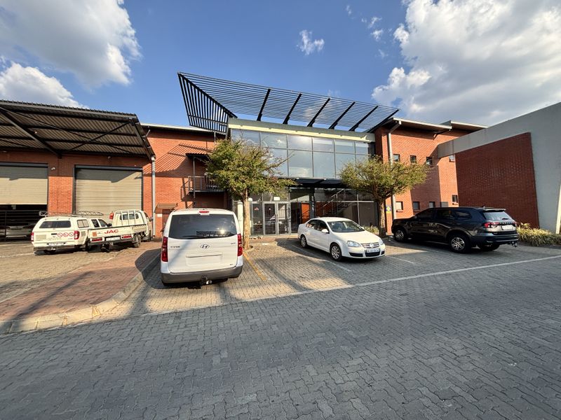 Front elevation of an industrial property featuring a brick facade, large glass entrance, metal canopy, and a paved parking area with roller shutter access.