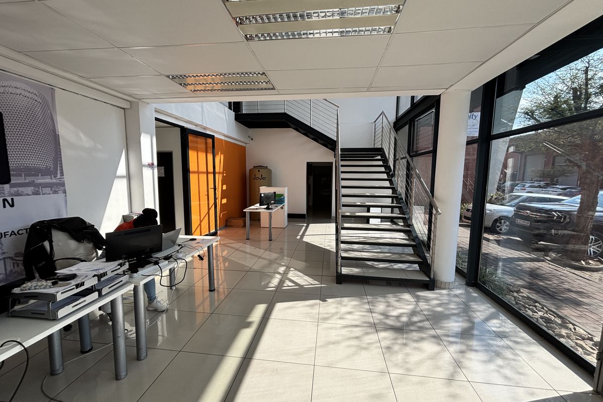 Spacious industrial entrance area featuring tiled flooring, a modern metal staircase, and large glass windows providing ample natural light.