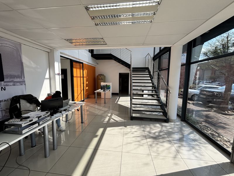 Spacious industrial entrance area featuring tiled flooring, a modern metal staircase, and large glass windows providing ample natural light.