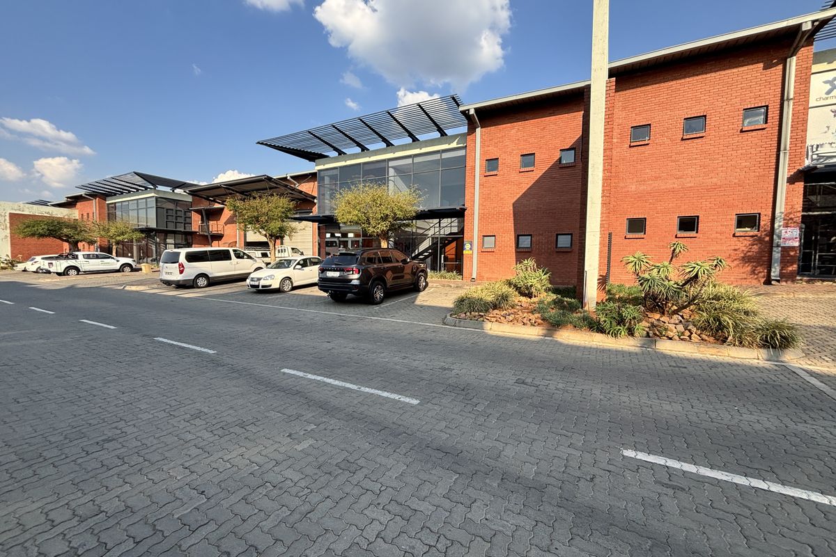 Front exterior view of an industrial complex featuring a red brick facade, glass curtain walling, and a paved parking area.
