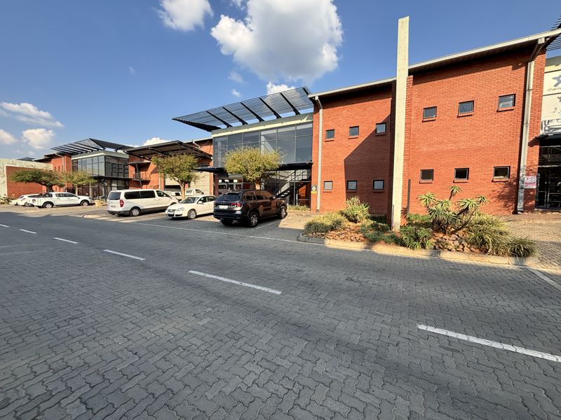 Front exterior view of an industrial complex featuring a red brick facade, glass curtain walling, and a paved parking area.
