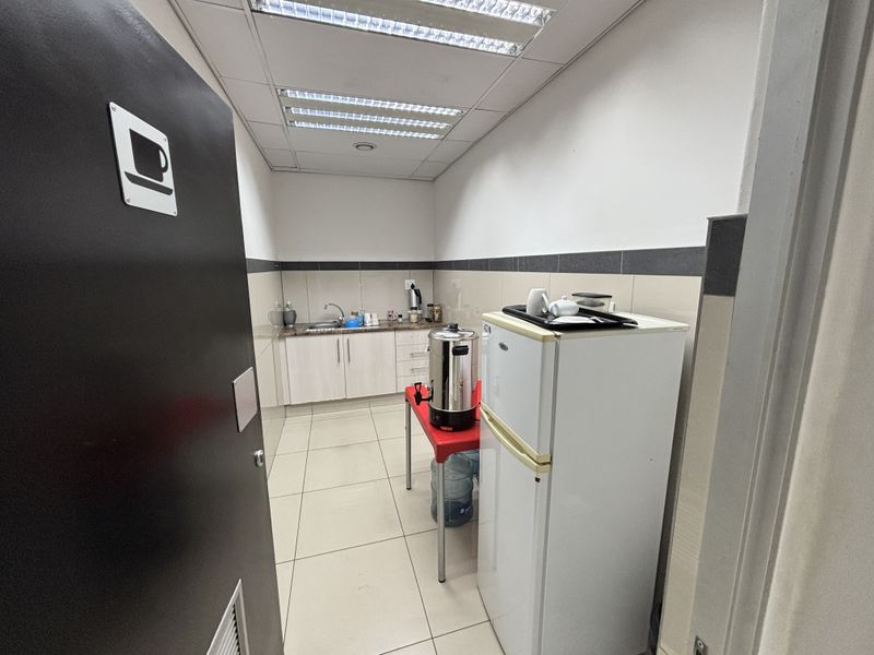 A functional industrial kitchenette featuring built-in cabinetry, a stainless steel sink, tiled backsplash, and overhead fluorescent lighting.