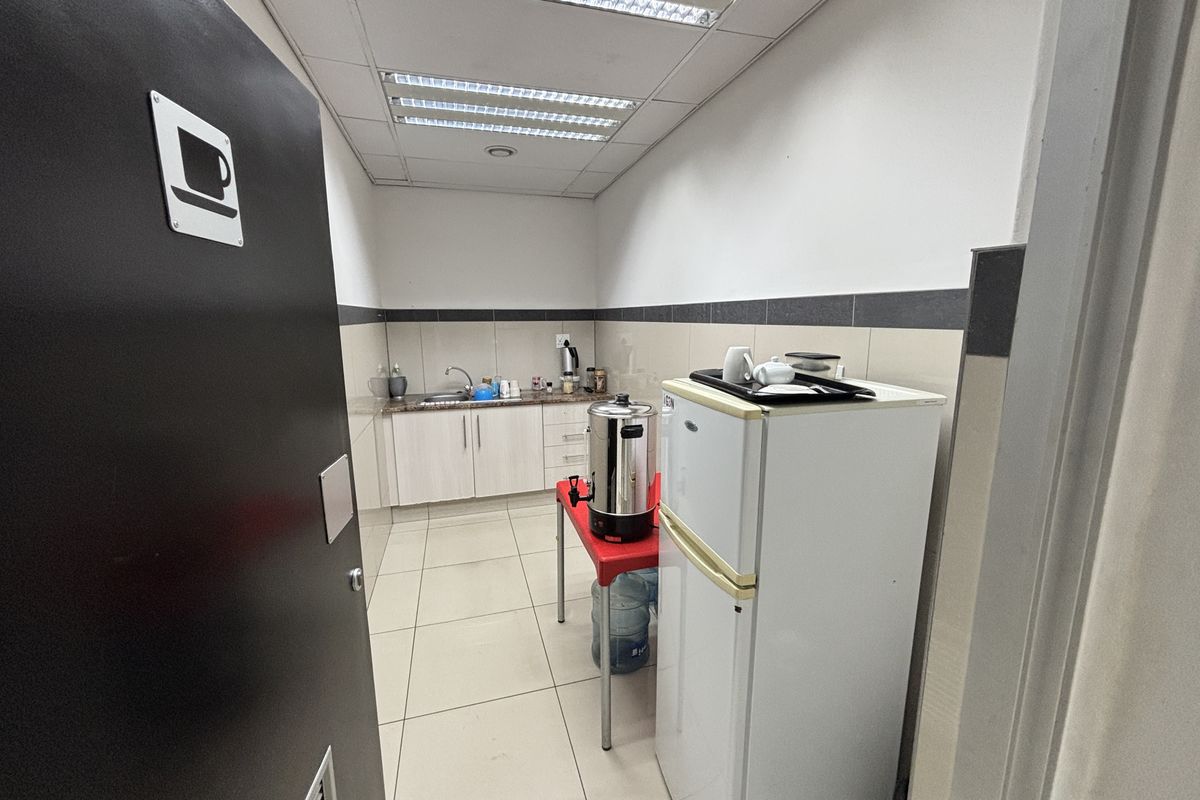 A functional industrial kitchenette featuring built-in cabinetry, a stainless steel sink, tiled backsplash, and overhead fluorescent lighting.