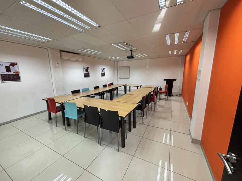 A functional office or meeting room featuring ceramic tiled flooring, a suspended ceiling with recessed lighting, and a wall-mounted air conditioning unit.